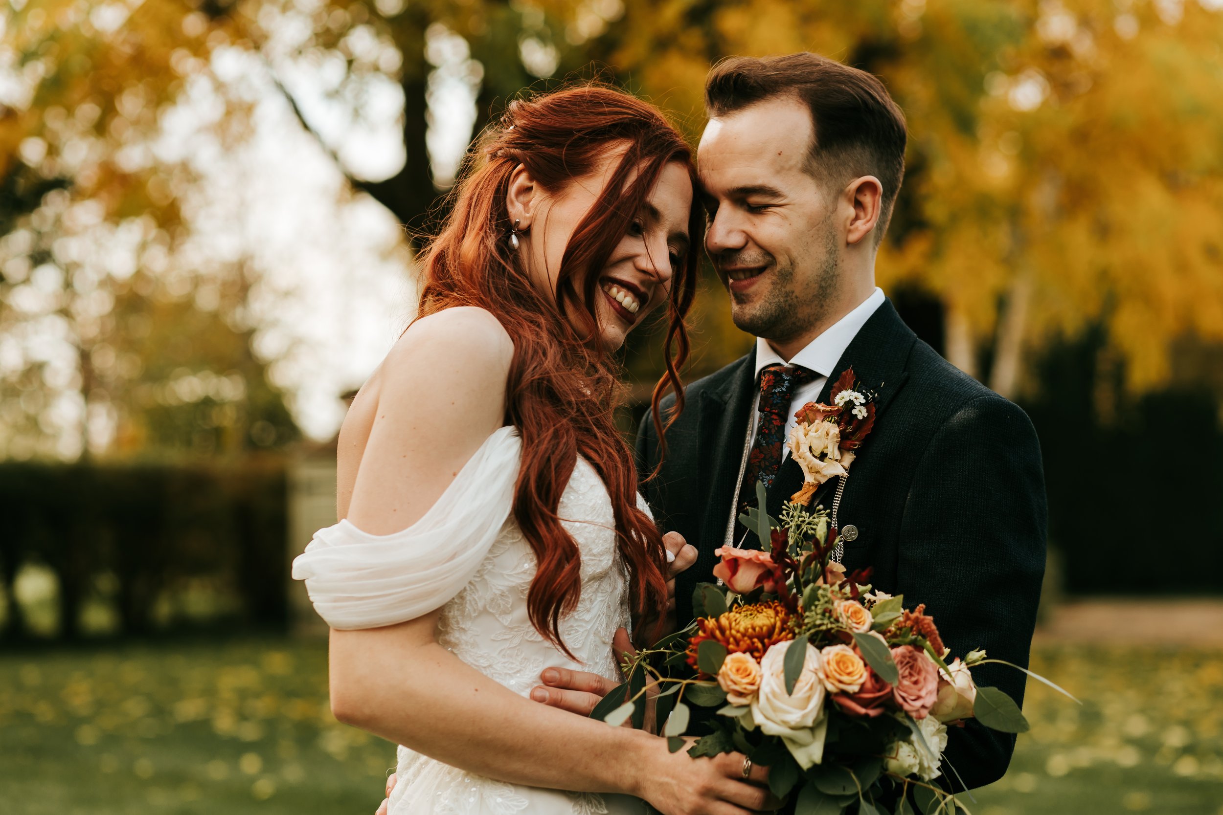 Happy couple in wedding attire embracing outdoors at South Farm Wedding Venue with autumn trees in background